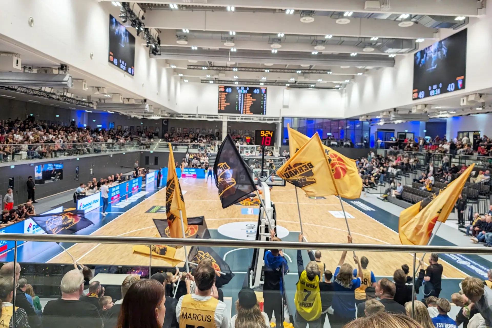 Voller Innenraum einer Sportarena mit vielen Zuschauenden bei einem Basketballspiel.