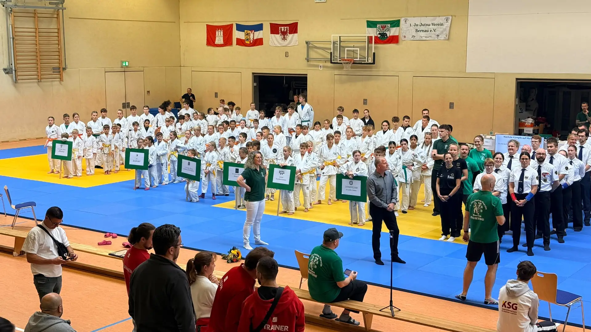 Mehrere Sportlerinnen und Sportler im Judogi/Trainingsanzug kämpfen bei einem Ju-Jutsu-Turnier in einer Sporthalle.